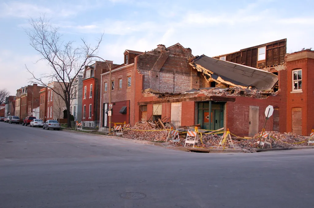 Partially collapsed corner brick building behind barriers.