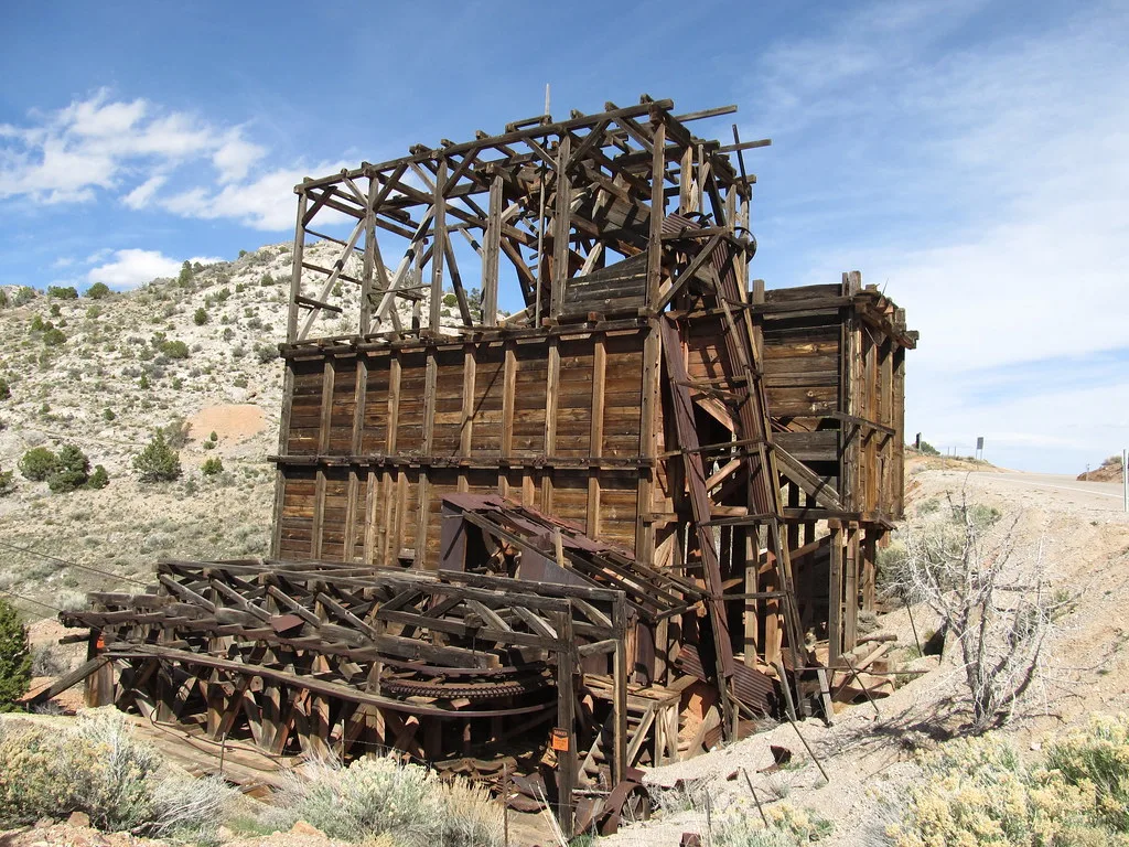 Ruined wooden industrial installation with a bare frame and rusty machinery on an arid slope.