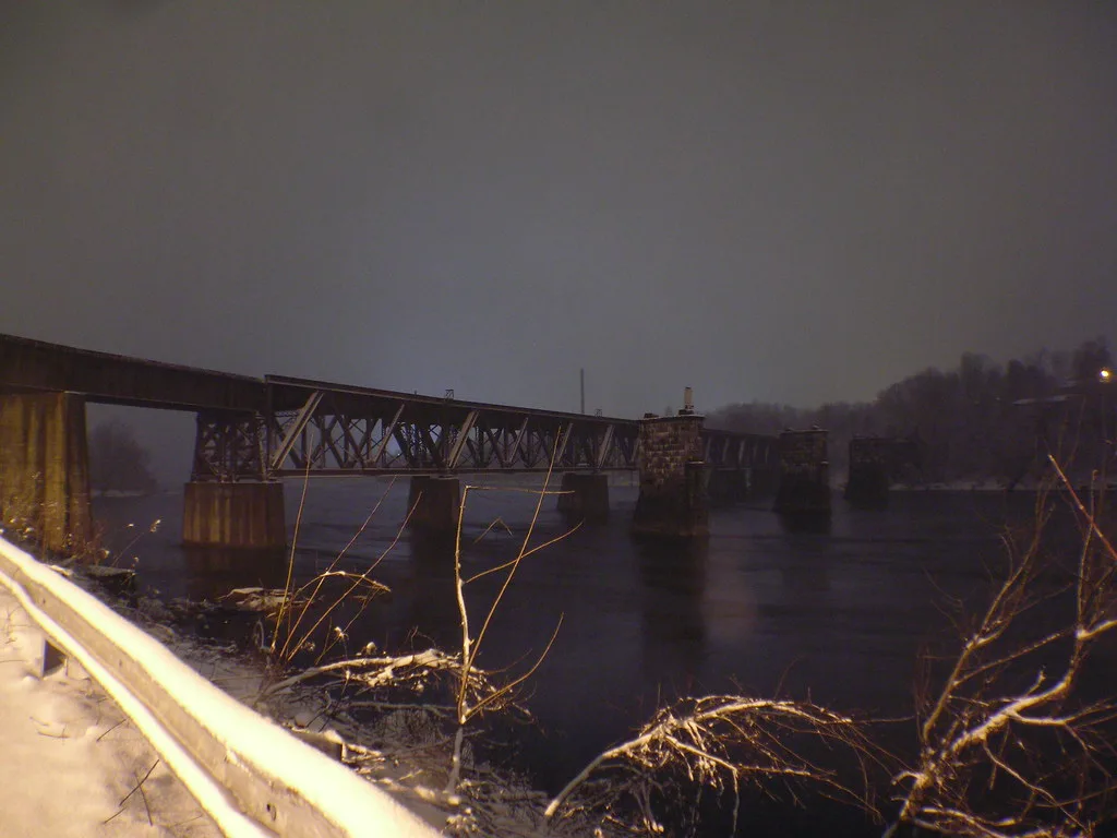Partly interrupted old metal bridge over a river at dusk.