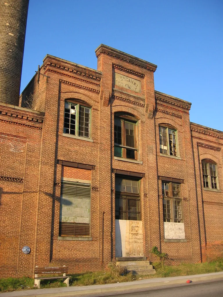 Old brick industrial facade with broken windows and a boarded door.