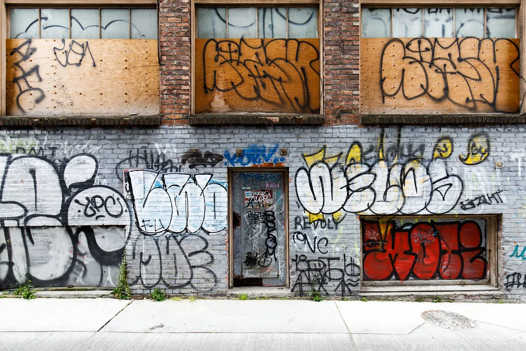 Graffiti-covered brick facade with boarded windows.
