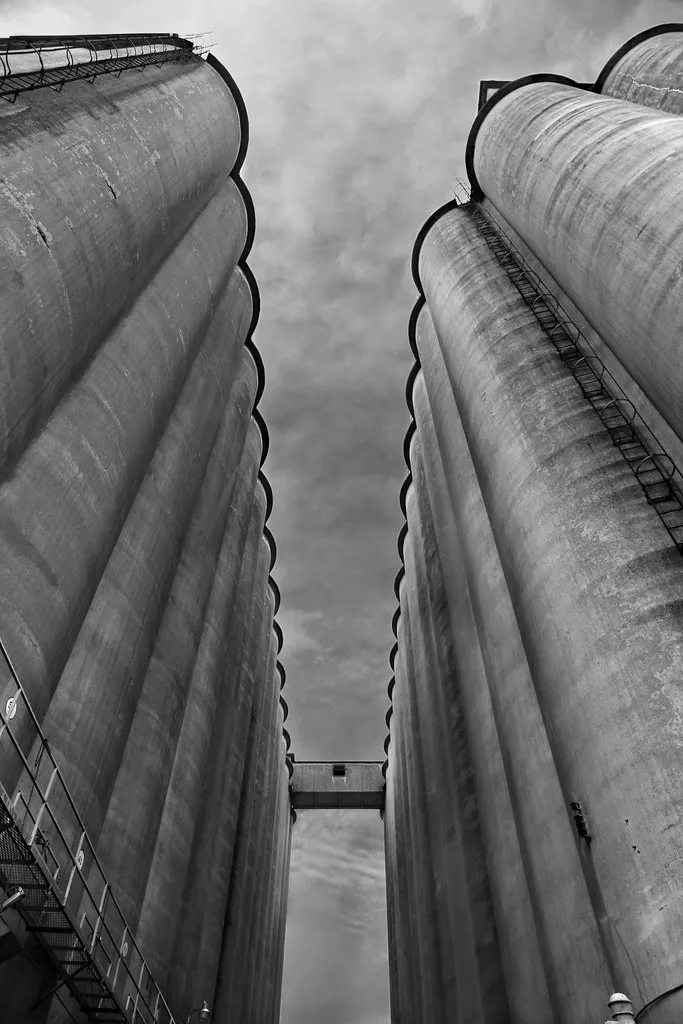 Concrete silos seen from below with an elevated connecting walkway.