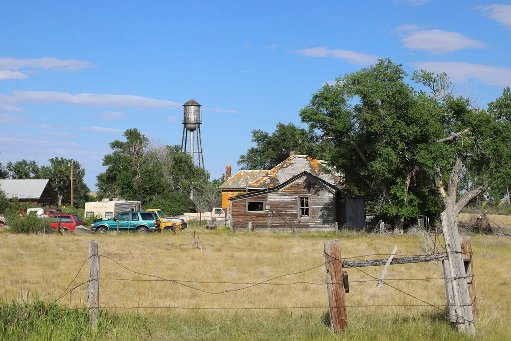 Deteriorated old wooden house near vehicles and a water tower.