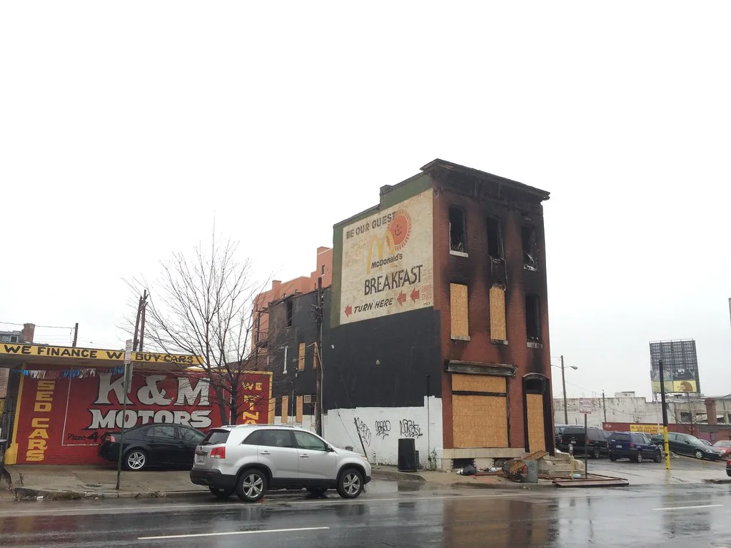 Blackened brick building with gaping upper windows and sealed lower openings.