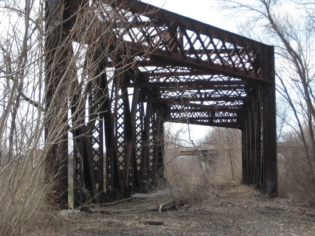 Abandoned old railway bridge with cross-braced metal beams, without rails and overgrown with saplings.