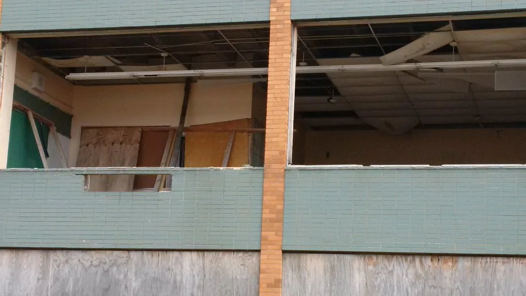 Abandoned rooms open to the outside with a collapsed suspended ceiling and boarded doors.