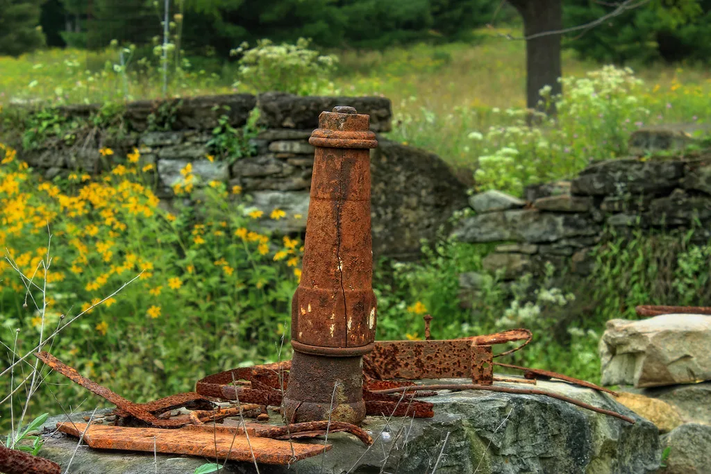 Rusty metal element in front of ruined stone walls.