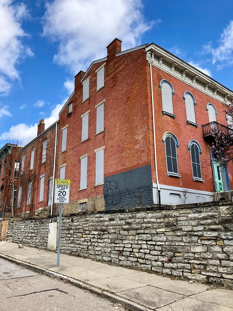 Large brick building with boarded windows above a stone wall.