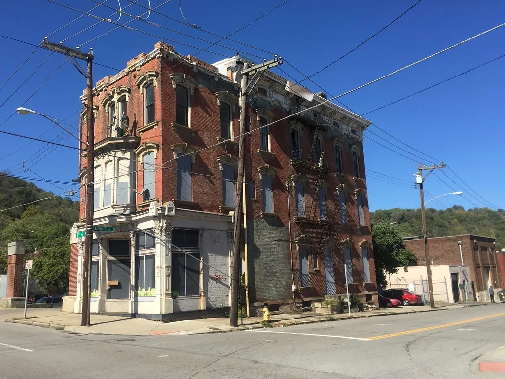 Abandoned red-brick corner building with boarded windows and a rusty fire escape.