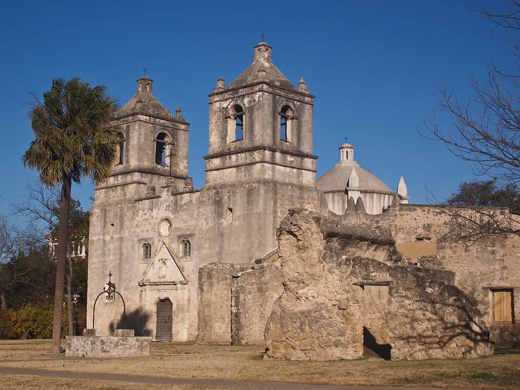 Masonry ruins in front of an old church with two bell towers.