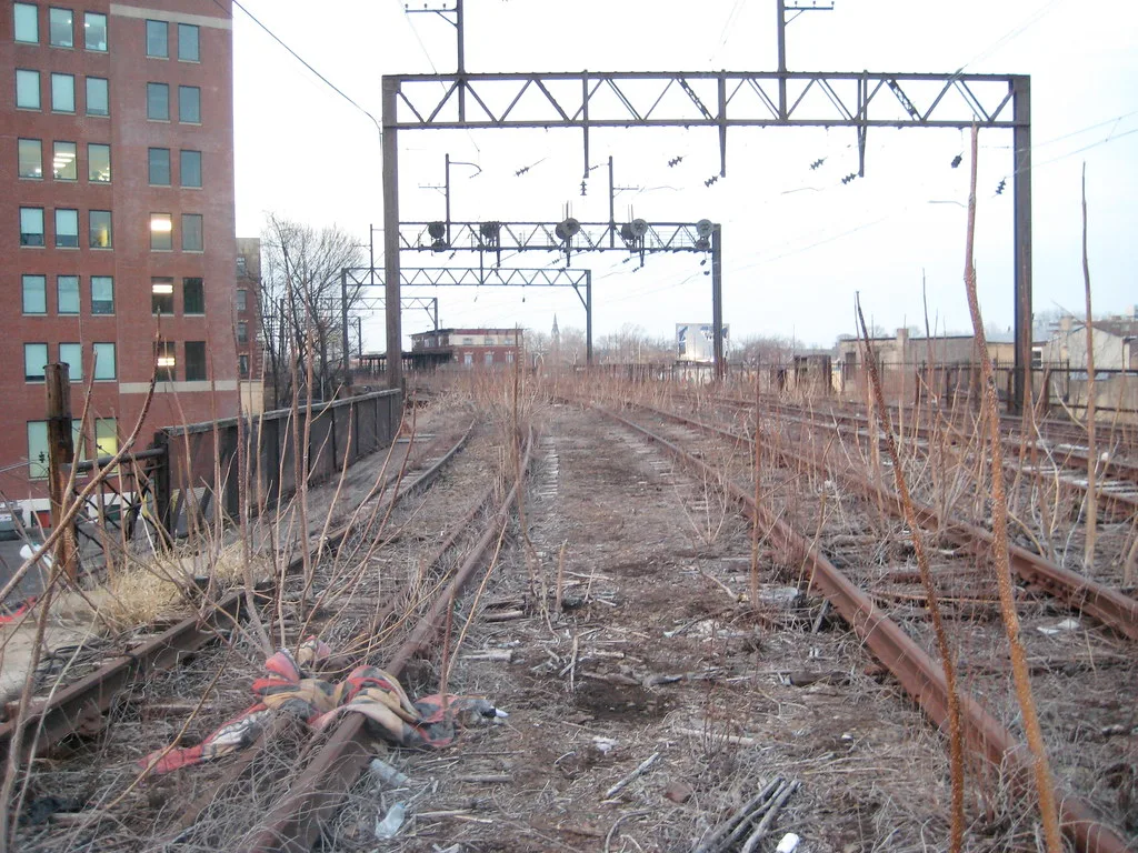 Overgrown former elevated railway tracks beneath overhead wire gantries.