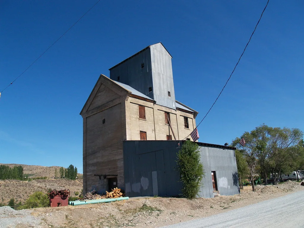 Old pale grain elevator with boarded windows and a blue metal extension.