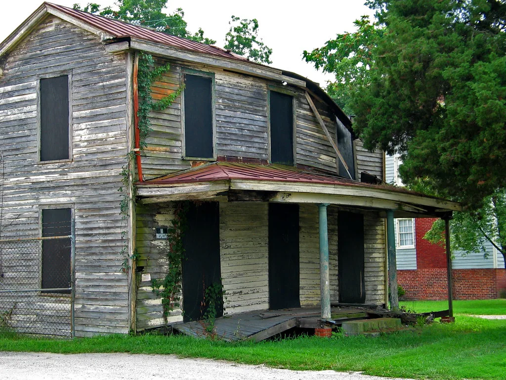 Boarded wooden house with a collapsed porch floor and peeling siding.