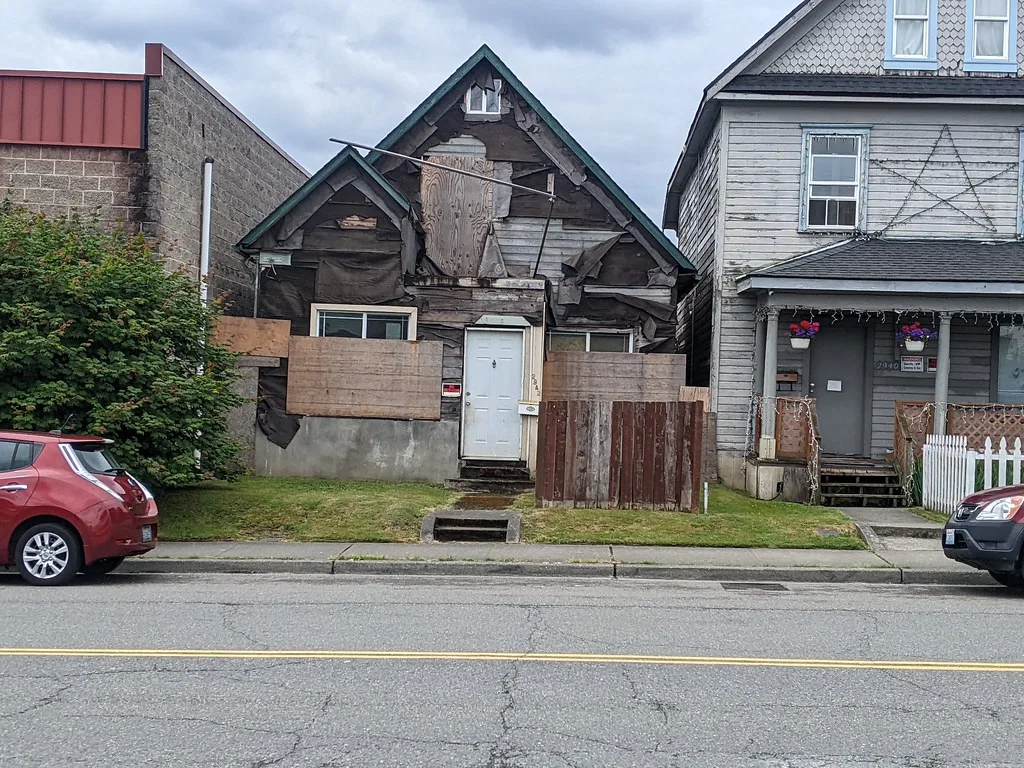 Small house with stripped gables and barricaded windows between two buildings.