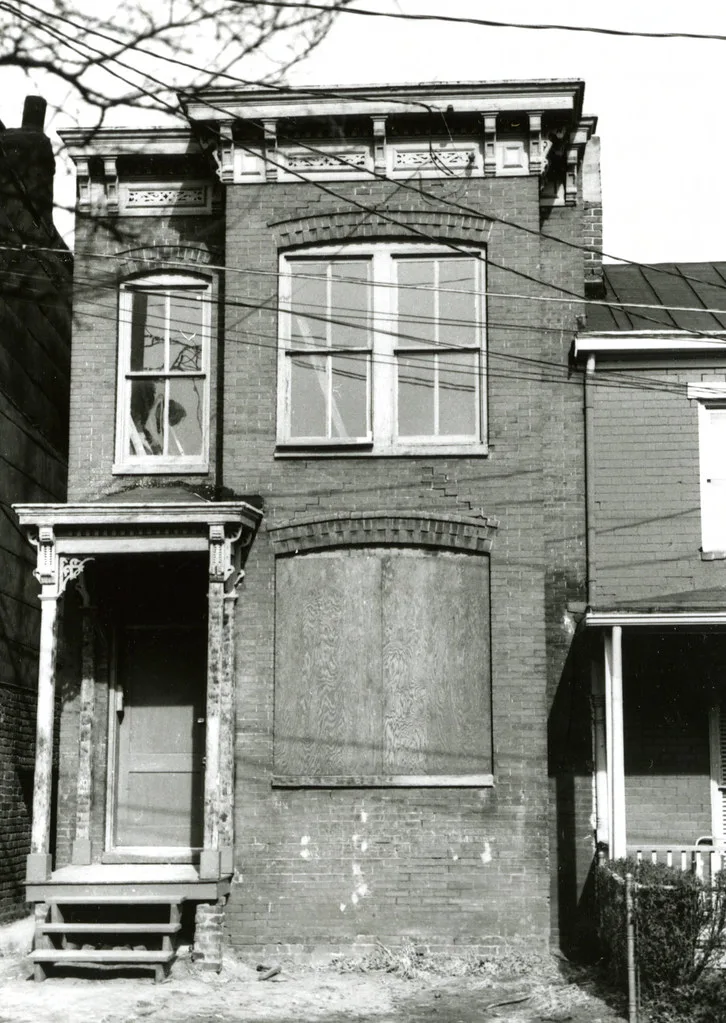 Brick house with broken and boarded windows, in black and white.