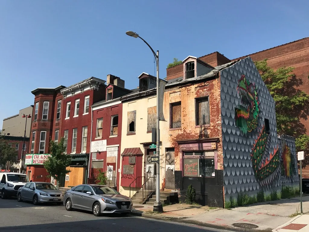 Vacant buildings with boarded openings and a mural on the side wall.
