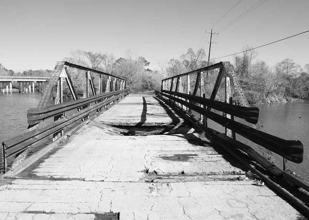 Old metal bridge with a large collapse in its deck, in black and white.
