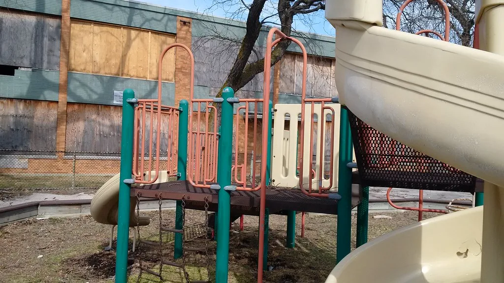 Slide and play platform before the boarded windows of a derelict building.