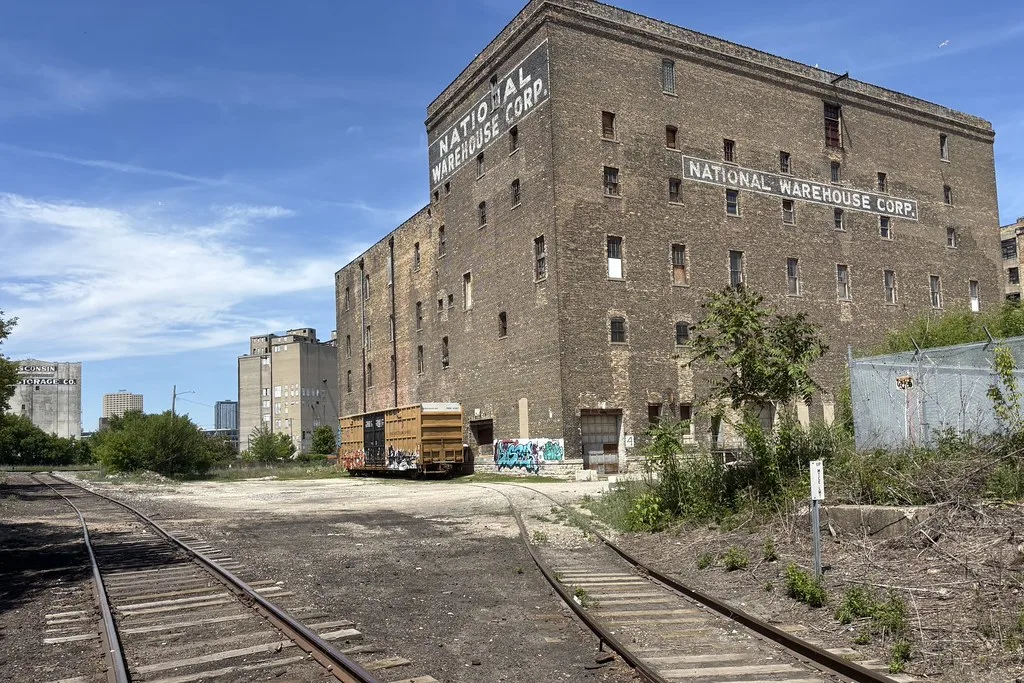 Old brick warehouse with deteriorated windows beside railway tracks.