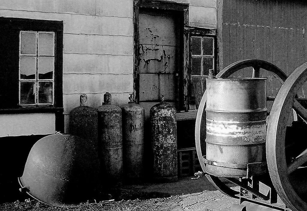 Metal cylinders and old wheels outside a decaying workshop.