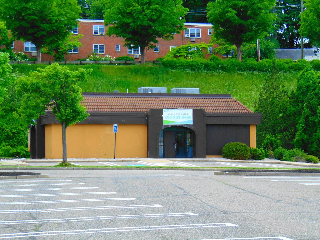 Old restaurant with boarded windows beside an empty parking lot.