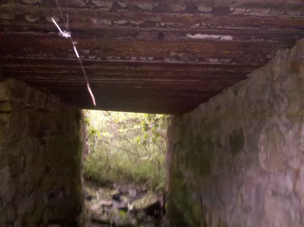 Old passage between stone walls beneath a deteriorated covering.