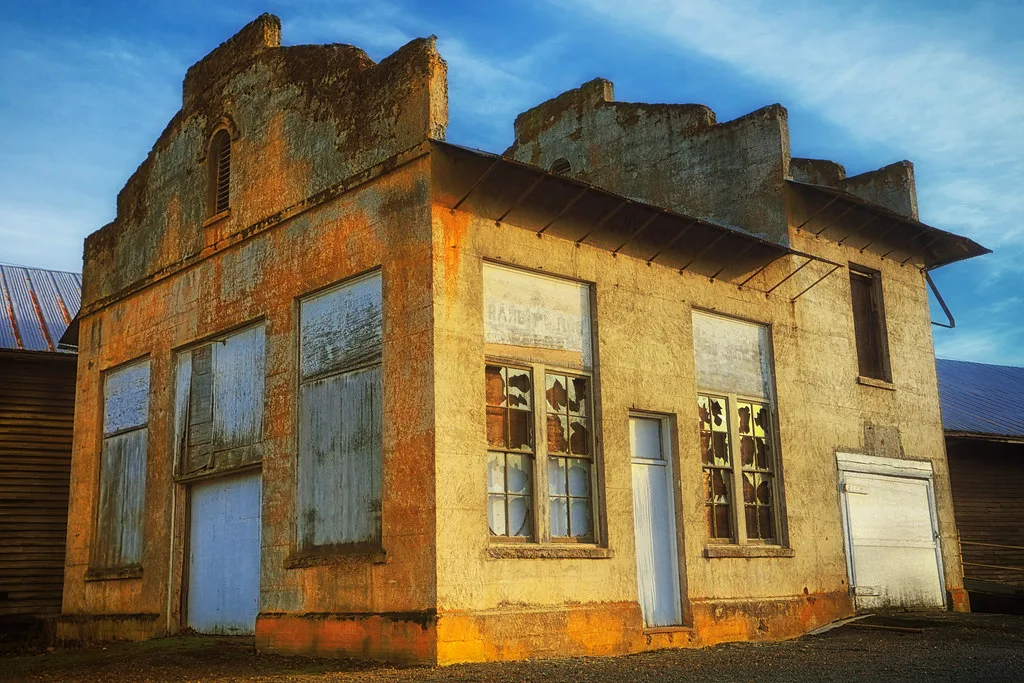 Old ochre-rendered building with broken windows and boarded openings.
