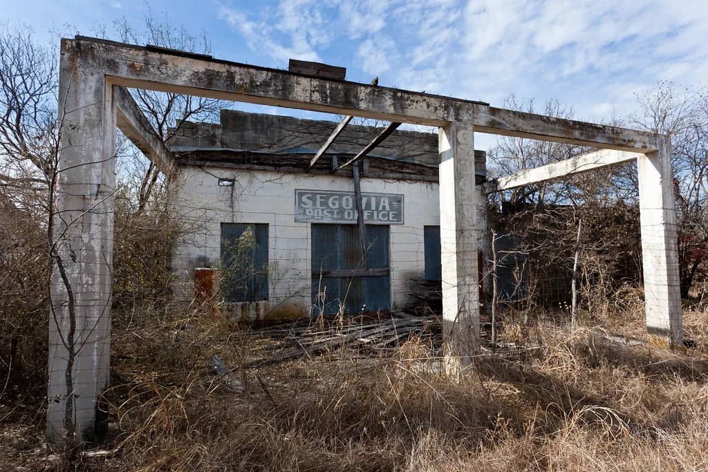Ruined old post office behind a bare canopy frame.