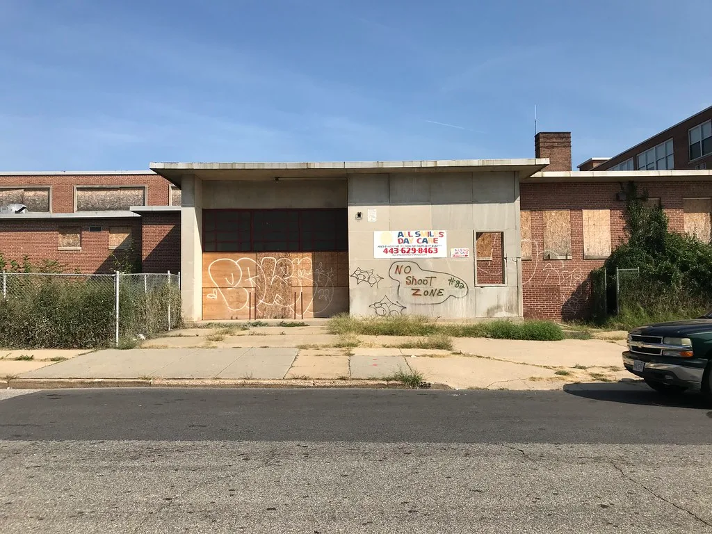Former brick school with boarded windows and a graffiti-covered entrance.