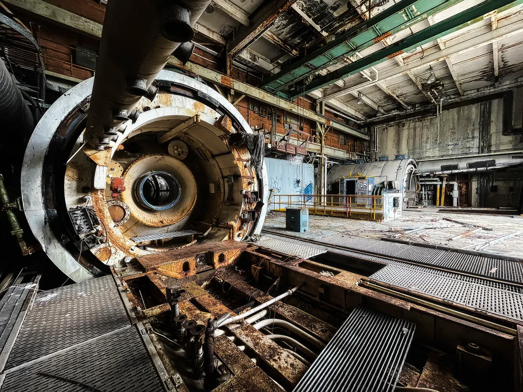 Large dismantled machine inside a deteriorated industrial hall.