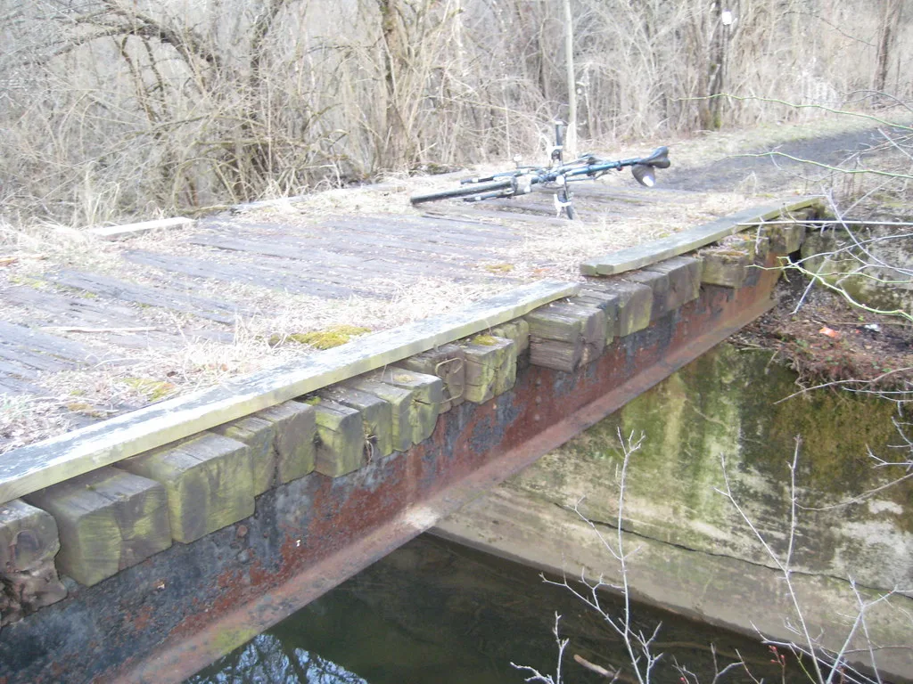 Old rusty metal bridge with a wooden deck and a bicycle resting on it.