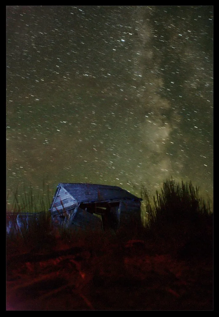 Dilapidated wooden barn beneath a starry sky.