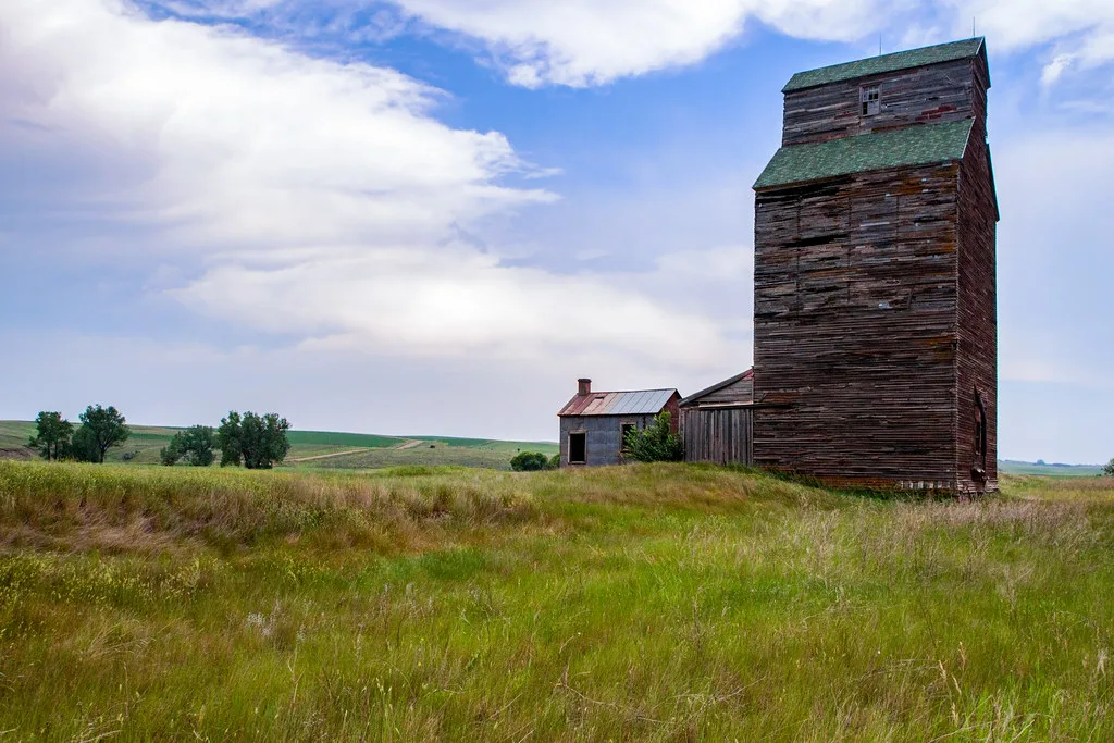 Old wooden elevator and small outbuilding in tall grass.
