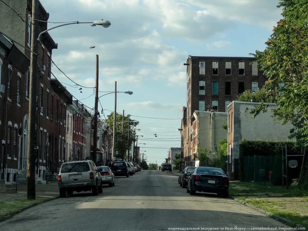 Rue bordée de maisons avec un ancien immeuble aux fenêtres vides sur la droite.