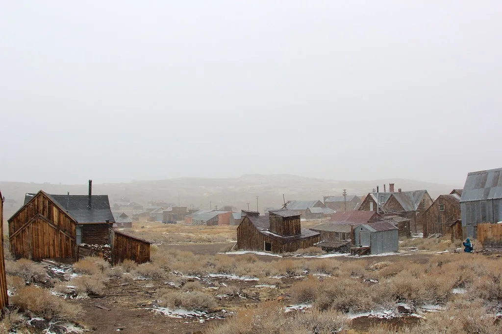 Old wooden buildings in a dry landscape beneath a misty sky.