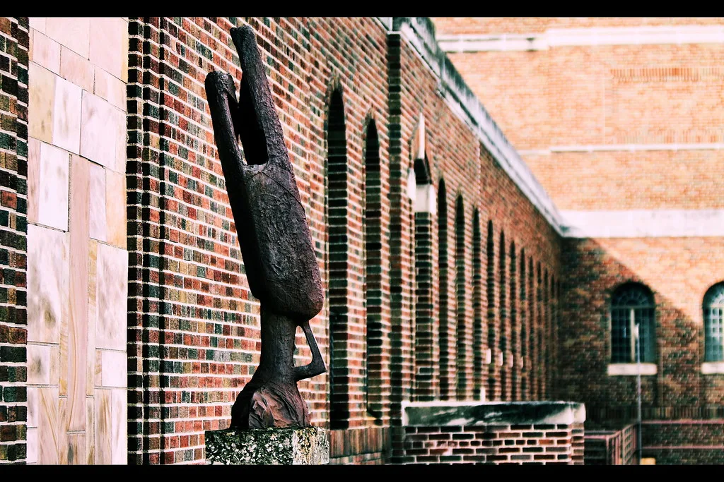 Dark sculpture in front of a neglected brick building with boarded windows.