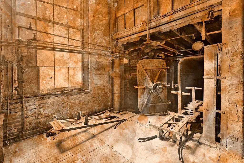 Interior of an old industrial workshop with pipes and debris on the floor.