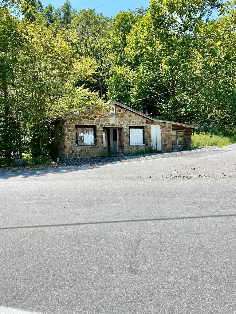 Small stone building with boarded windows beside a road.
