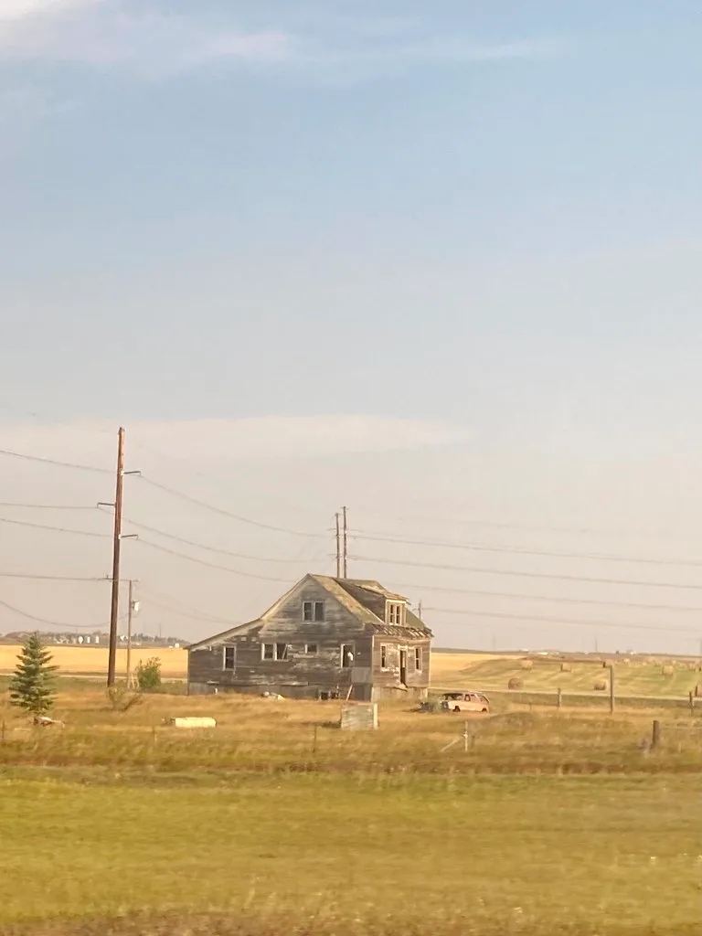 Abandoned wooden house with broken windows in dry fields beneath power lines.
