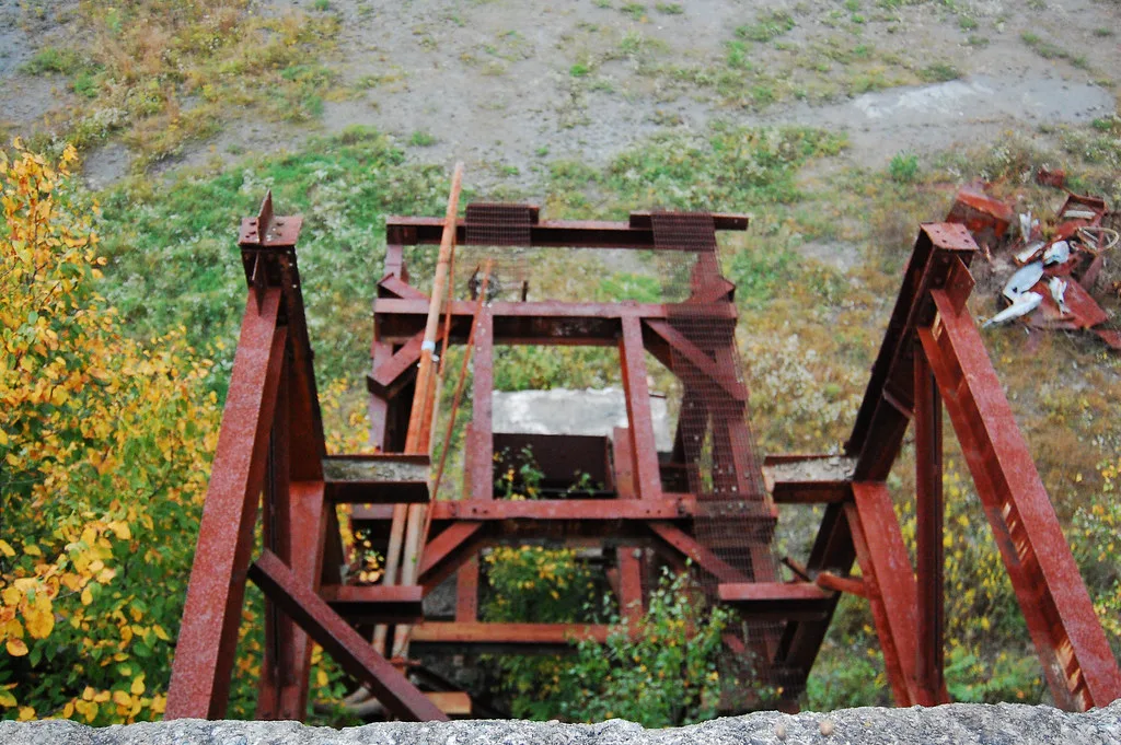 Rusty steel framework of a disused industrial installation seen from above amid vegetation.
