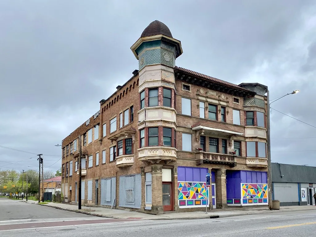 Old turreted building with boarded windows and painted shopfront panels.