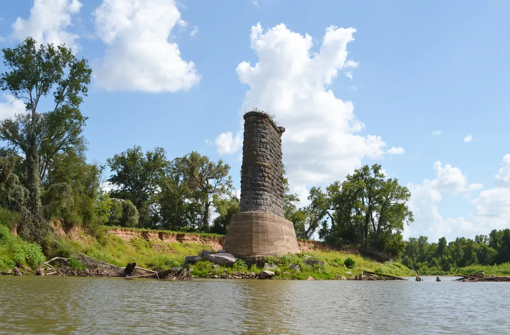Isolated old stone bridge pier beside a river.