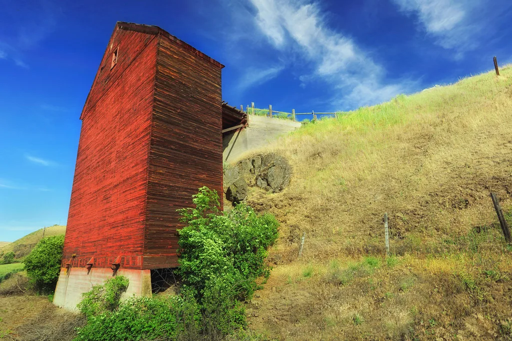 Old red wooden tower against a grassy hillside.