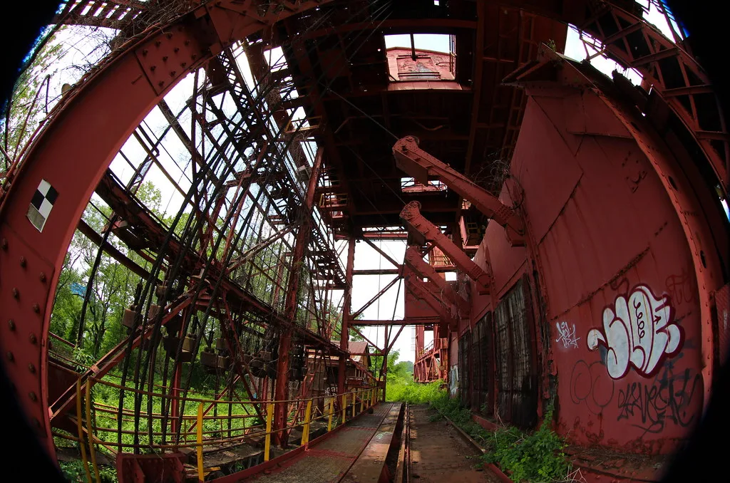 Structure industrielle rouge envahie de végétation, vue au grand-angle.