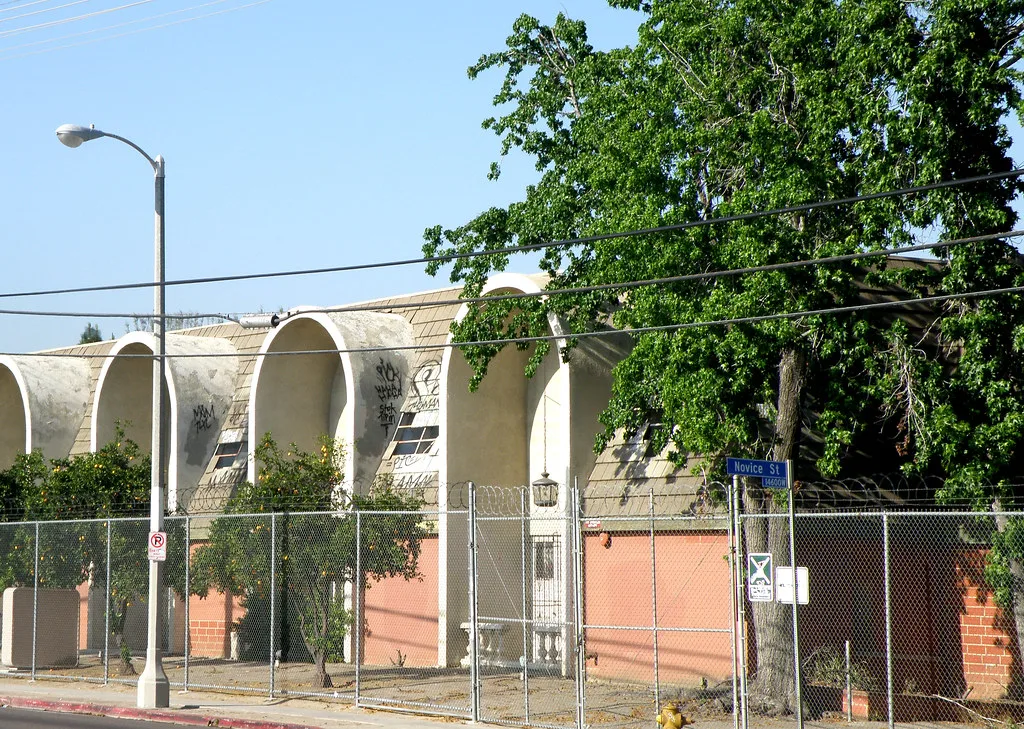 Ancien bâtiment aux grandes arches et fenêtres dégradées derrière une clôture.