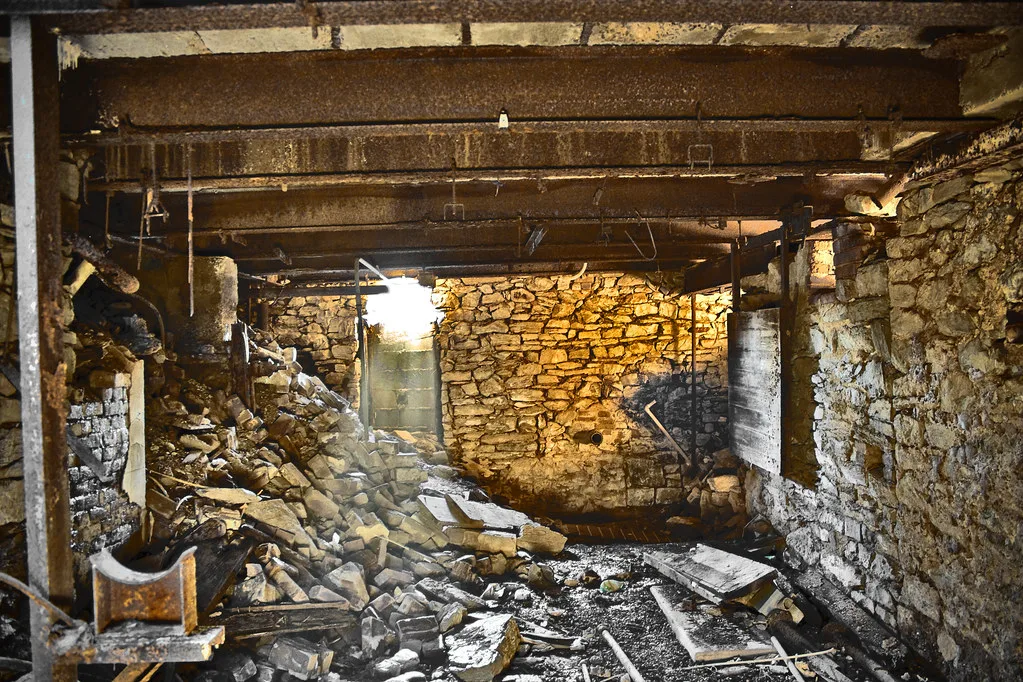 Ruined interior with stone walls, rusty beams and rubble.