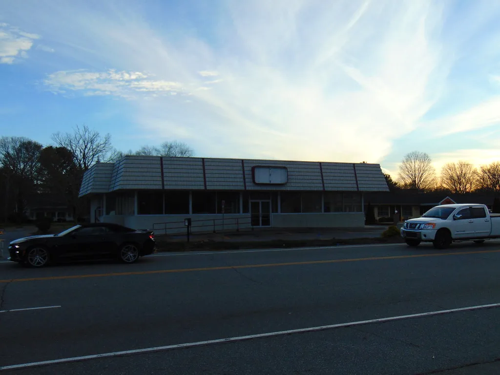 Dark facade of a former shop with its sign removed beside a road.