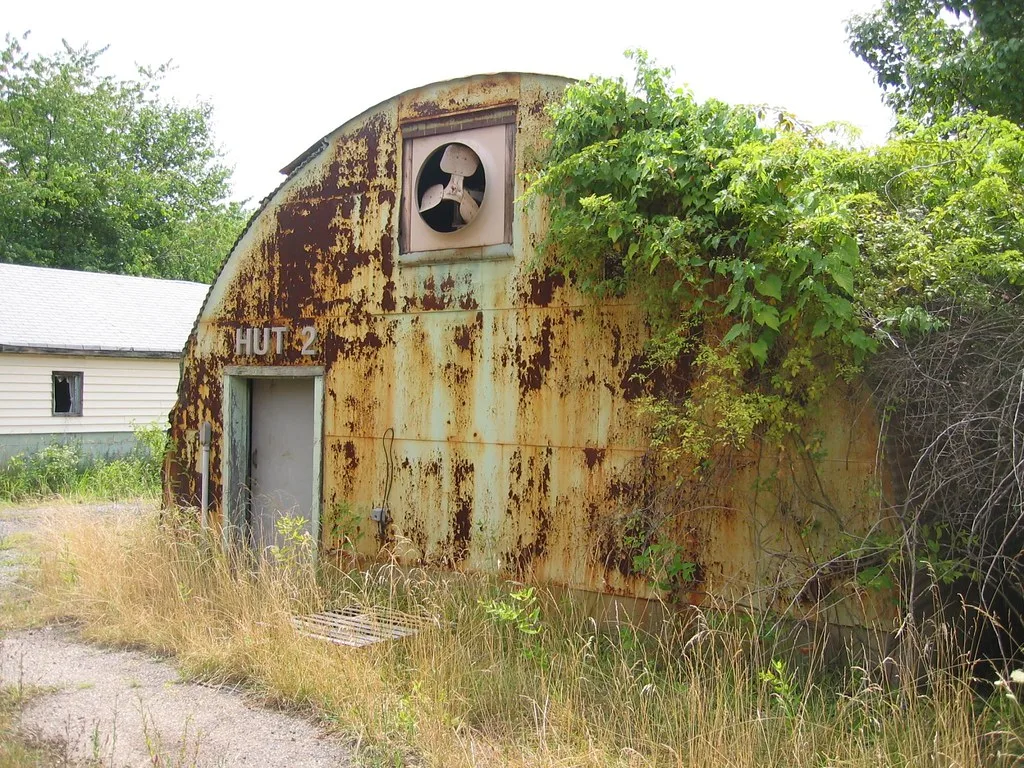 Old rounded metal shed, rusty and overgrown with vegetation.