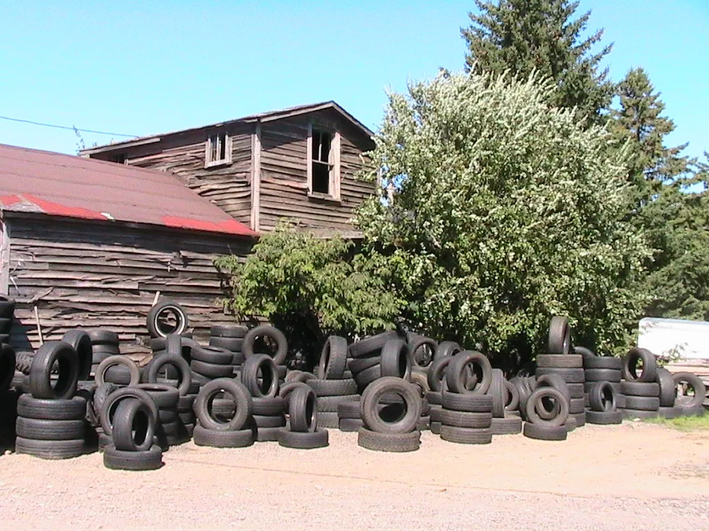 Dilapidated wooden building behind stacks of tires.