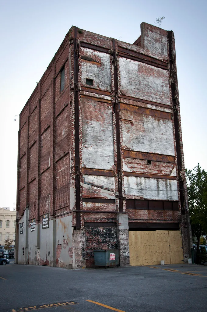 Tall brick warehouse with bricked-up openings and rusty structural elements.